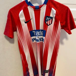 Atletico Madrid (Griezmann) t-shirt hemma 2018/19 i storlek 152 - Säljer en Atletico Madrid Med Griezmann på ryggen från 2018! Den är bra skick förutom att laliga loggan på armen har lossnat lite. Jag säljer den för 150kr!