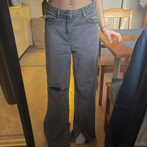 Grå jeans med slits Bershka - Säljer ett par grå jeans med medel midja och vida ben. De har en cool slits vid anklarna och ett hål på ena benet för en edgy look. Perfekta för en avslappnad stil. OPS: Dom är långa i längd, är 163cm och går långt över mina fötter.