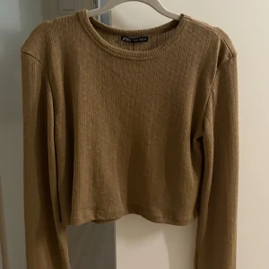 Beige ribbad croppad tröja från Zara - Säljer en beige ribbad tröja från Zara. Den är croppad med långa ärmar och har en rund halsringning. Den är i storlek L men jag bär S kläder och ni ser hur den sitter på mig. Den har fortfarande prislappen på så aldrig använd💕
