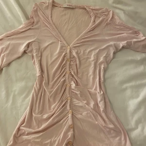 Ljusrosa blus från Zoul - Säljer en ljusrosa blus från Zoul med knappar framtill och v-ringad design. Blusen  har långa ärmar och är tillverkad i ett mjukt material som ger en bekväm passform.