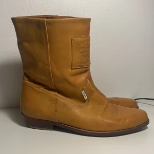 Bruna boots från Levis - Snygga bruna, äldre boots i skinn från Levis med en klassisk design. De har en fyrkantig tå och en diskret logotyp på sidan. Perfekta för en stilren look. De är små i storleken, står 42 men är mer 41 1/2