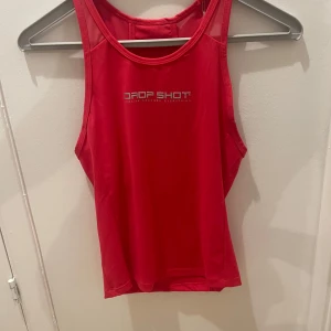 Röd linnetopp från Drop Shot - Snygg röd linnetopp från Drop Shot med sportig design. Perfekt för träning med sitt lätta och bekväma material. Toppen har en rund halsringning och är ärmlös för maximal rörelsefrihet.
