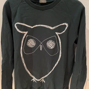 Mörkgrön tröja med ugglemotiv från Knowledge Cotton Apparel - Säljer en mörkgrön tröja från Knowledge Cotton Apparel med ett coolt vitt ugglemotiv på framsidan. Tröjan har långa ärmar och ribbade muddar vid ärmslut och nederkant. Perfekt för en avslappnad stil!