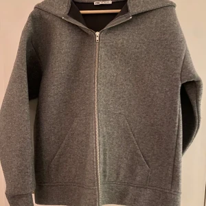 Grå jacka från Zara - Snygg och bekväm grå jacka från Zara med dragkedja framtill. Perfekt för kyliga dagar med sin mjuka och varma känsla. Den har en klassisk design med långa ärmar och en praktisk huva.