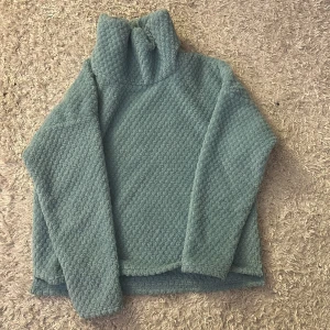 Turkos fleece tröja från Everest - Mysig turkos fleece tröja från Everest med hög krage. Perfekt för kyliga dagar med sin mjuka och varma känsla. Tröjan har långa ärmar och en texturerad yta som ger extra stilpoäng.
