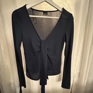 Svart långärmad topp från Gina Tricot -  svart långärmad topp från Gina Tricot med knytning framtill. Toppen har en djup v-ringning och är i ett mjukt material.