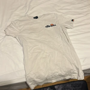 Vit t-shirt från Ellesse - Säljer en klassisk vit t-shirt från Ellesse med logga på bröstet. Perfekt för en avslappnad stil. T-shirten har korta ärmar och en rund halsringning.