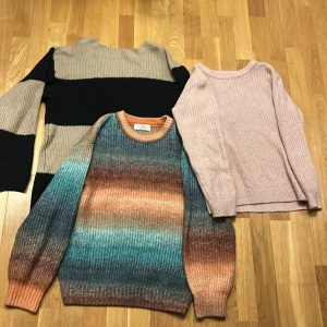 Tre stickade tröjor från H&M och 157 - Säljer tre stickade tröjor. En från H&M i flerfärgat mönster med nyanser av blått, orange och brunt. Två från 157, en randig i beige och svart, och en i ljusrosa. Alla har långa ärmar och ribbade detaljer.