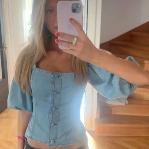 Ljusblå jeanstopp  - Trendig denim jeanstopp med knappar framtill och puffiga trekvartsärmar. Helt perfekt inga defekter