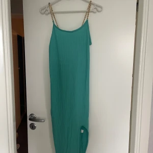 Turkos långklänning med kedjeband - Snygg turkos långklänning med kedjeband som ger en unik touch. Klänningen har en ribbad struktur och är perfekt för sommarens festligheter. Den är ärmlös och har en elegant passform.
