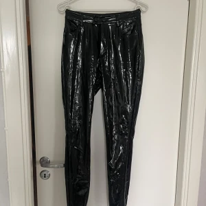 Svarta glansiga byxor från FB Sister - Snygga svarta glansiga byxor från FB Sister i storlek XS. Byxorna har en tight passform och är perfekta för en trendig look. De har en hög midja och är tillverkade i ett syntetmaterial som ger en cool, blank yta. 