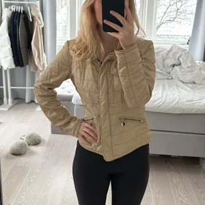 Beige quiltad jacka från Moncler - Snygg beige quiltad jacka från Moncler med dragkedja och knappar. Jackan har en normal passform och långa ärmar. Perfekt för höst och vår. Den är i bra skick. Finns även en luva man kan sätta på och ta av, den är i samma material och design som resten av jackan. passar xs och s