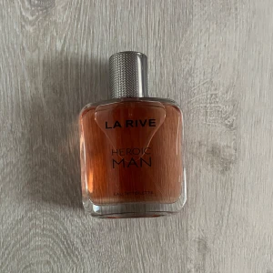 La Rive Heroic Man Eau de Toilette 100ml - Säljer en flaska La Rive Heroic Man Eau de Toilette. Flaskan har en stilren design med en metallisk kork och en varm, bärnstensfärgad vätska. Perfekt för den som vill ha en maskulin och fräsch doft. 100 ml
