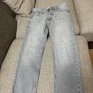 Grå jeansbyxor från jack & Jones  - Snygga grå jeansbyxor i relaxed fit. Perfekta för en avslappnad stil med klassisk femficksdesign och knappgylf. Passar bra till både vardag och mer avslappnade tillfällen.