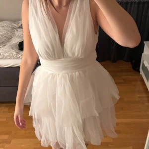 Vit ärmlös klänning med volang - Elegant vit klänning med djup v-ringning och volangdetaljer. Helt ny med lappen kvar. Perfekt till student eller skolavslutning 
