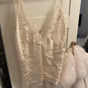 Beige satinlinne från Zara - Säljer ett elegant beige satinlinne från Zara med spetsdetaljer vid halsringningen. Linnet har justerbara axelband och en mjuk, glansig yta som ger en lyxig känsla. Perfekt för en stilren look. Köptes för 469kr.