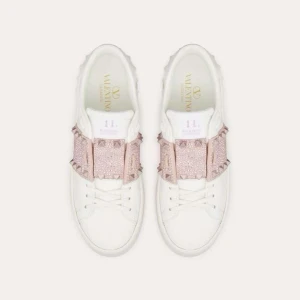 Valentino sneakers med rosa paljettdetaljer - Stilrena vita sneakers från Valentino med glittriga rosa paljettdetaljer över snörningen. Perfekta för att ge din outfit en lyxig touch.