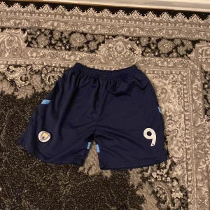 Mörkblå fotbollsshorts med nummer 9 - Snygga mörkblå fotbollsshorts med ljusblå detaljer och nummer 9 tryckt på framsidan. Perfekta för fotbollsträningen eller matchen.