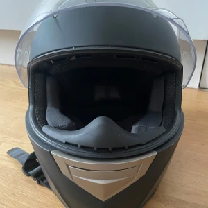 Viarelli mopedhjälm storlek m - Mopedhjälm från Viarelli med klart visir. Hjälmen har en aerodynamisk design och ventilationsöppningar, godkänd E9. Aldrig av ramlad med eller tappad, några skrapsår från mopedens sits när man stänger. Sparsamt använd. Nypris 1299kr