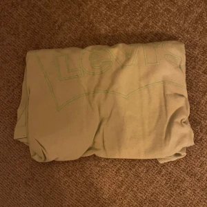 Grön t-shirt från Levi's - Säljer en grön t-shirt från Levi's med deras ikoniska logga tryckt på framsidan. T-shirten är kortärmad och tillverkad i ett mjukt bomullsmaterial. Perfekt för en avslappnad stil.