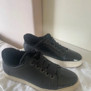 Svarta sneakers från Billibi - Snygga svarta sneakers från Billibi med snörning och en vit sula. Skorna har en stilren design med en glansig finish och är perfekta för en avslappnad look.