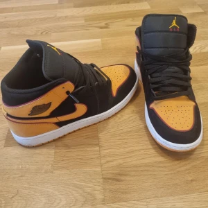 Nike Air Jordans i svart och orange - Snygga Nike Air Jordans i svart och orange med klassisk snörning. Perfekta för dig som vill ha en stilren och sportig look. Skorna har en vit sula som kontrasterar snyggt mot det färgglada mönstret.