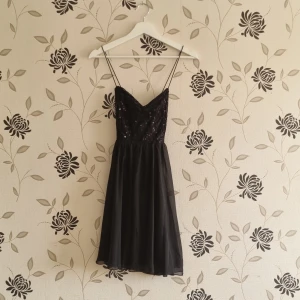 Svart paljettklänning från Nly One, Strl: 36, nyår, lappar kvar - Elegant svart klänning med smala axelband och paljettprydd överdel. Kjolen är lätt och fladdrig, perfekt för en festlig kväll. Klänningen har en v-ringad design som ger en stilren look. Nly One, lappar kvar se bilder.