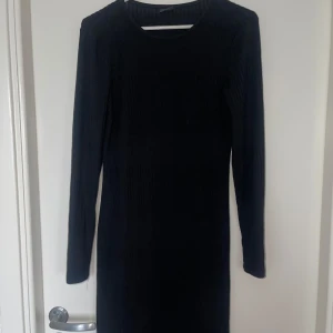 Svart ribbad klänning från Gina Tricot - Snygg svart ribbad klänning från Gina Tricot i storlek S. Klänningen har en enkel och stilren design med långa ärmar och rund halsringning. Perfekt för en elegant och bekväm look.