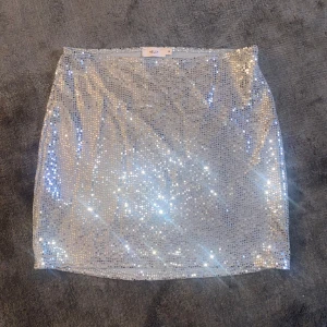 Glittrig kjol från Nelly - Snygg och glittrig kjol från Nelly. Kjolen har en kort längd och en tight passform.