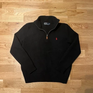 Svart quarter zip tröja från Ralph Lauren - Säljer en snygg svart quarter zip tröja från Ralph Lauren med en röd logga på bröstet. Tröjan har en hög krage och är perfekt för kyligare dagar. Det står att tröjan är i Storlek M men den passar som S då den krympt lite. Väldigt skönt och tjockt material! 