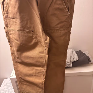 Carhart byxor - Carhart double knees. Sitter lite löst o är i bra skick. Lite slitningar vid fötterna