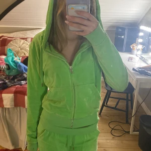 Grön hoodie från Juicy Couture - Säljer en snygg grön hoodie från Juicy Couture med dragkedja och huva. Den har en dekorativ J-detalj vid dragkedjan och är tillverkad i ett mjukt material. Perfekt för en avslappnad stil.