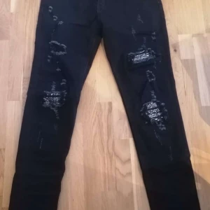Svarta jeans från Amiri - Snygga svarta jeans från Amiri med slitna detaljer. De har en klassisk femficksdesign och en knappgylf. Perfekta för en trendig look. Nästan oanvända