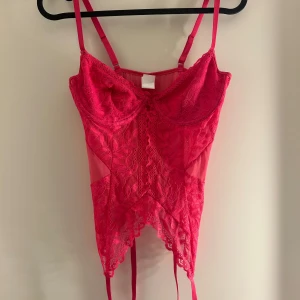 Rosa spetskorsett - Snygg rosa  korsett med spetsdetaljer och justerbara axelband. Perfekt för en festlig kväll eller speciella tillfällen. 