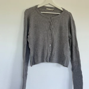 Grå ribbad kofta från Uniqlo - Säljer en superfin grå ribbad kofta. Den är i storlek L och har en klassisk rund halsringning. Koftan har långa ärmar och knäpps med små knappar framtill. Perfekt för höst och vinter, och den är i nyskick! 🩶