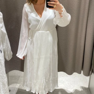 Vit omlottklänning - Säljer en superfin vit omlottklänning med långa ärmar och knytband i midjan. Klänningen är perfekt för sommar och vår, och den har en elegant och luftig design. Materialet känns lite tyngre men fortfarande bekvämt, vilket gör den idealisk för både vardag och fest. Passformen är normal och klänningen har en v-ringad hals. Nypris 600kr.