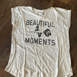 Grå t-shirt med text - Grå t-shirt med svart text och pärlor på. Sparsamt använd, och pärlorna sitter på ordentligt. 