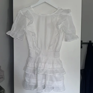 Vit klänning från Gina Tricot - Säljer en superfin vit klänning från Gina Tricot i storlek 146/152 men passar 134/140 också!Klänningen har korta ärmar och volangdetaljer. Den är perfekt för sommaren och midsommarfiranden. Klänningen är i nyskick och har en öppen rygg. Materialet är lätt och luftigt, perfekt om det är varmt.