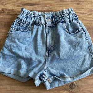 Blå jeansshorts med resårmidja - Säljer ett par snygga blå jeansshorts med resårmidja. De har en knapp och dragkedja framtill samt två fickor både fram och bak. Perfekta för sommaren! 🩳💙