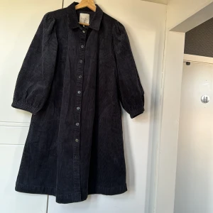 Klänning/kappa - Mörkblå manchester klänning med knappar framtill (kan även användas som kappa). Har fickor på båda sidorna. Väldigt stor i storleken, mer 40/42 skulle. Aldrig använd, nypris 2000kr Kom gärna med prisförslag