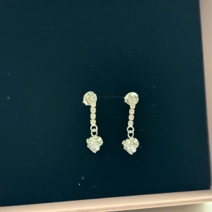 Silverörhängen med hjärtan och stenar - Säljer ett par eleganta silverörhängen med hängande diamant och gnistrande stenar. Perfekta för att lägga till lite extra glans till din outfit. Örhängena är i nyskick💕
