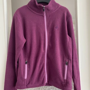Lila fleecejacka med dragkedja - Säljer en mysig lila fleecejacka med dragkedja framtill. Jackan har långa ärmar och två fickor med dragkedjor. Perfekt för kyliga dagar!