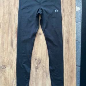 Svarta leggings med hög midja - Säljer ett par svarta leggings med hög midja. De är perfekta för träning och har en tight passform. Materialet är syntetiskt och de har en liten logga på ena benet. Superbekväma och i bra skick!