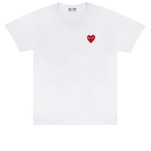 Vit t-shirt med rött hjärta från CDG - Säljer en snygg vit t-shirt från PLAY med ett rött hjärta på bröstet. T-shirten är kortärmad och gjord av bomull, perfekt för sommaren eller våren. Den har en relativt liten passform och är superbekväm att ha på sig. Passar både till vardags och fest!