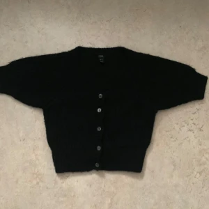 Svart kofta från Lindex - Säljer en svart kortärmad kofta från Lindex i storlek XS. Den har knappar framtill och är perfekt för både vardag och fest. Koftan är i ett mjukt material och har en klassisk design som passar till det mesta. Perfekt för höst och vinter 😊