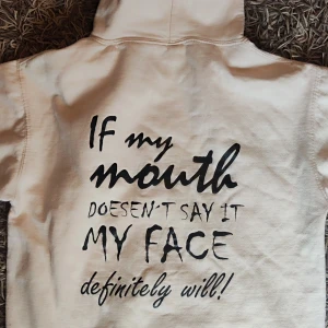 Vit hoodie från Just Hoodies  - Säljer en vit hoodie från Just Hoodies med ett kaxigt tryck på ryggen: 'If my mouth doesn't say it, my face definitely will!'. Perfekt för chill dagar.  Den har en stor ficka fram och en bekväm huva med dragsko. Använd 1 gång.  