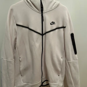 Nike Tech Fleece Tröja - Vit Nike tech fleece tröja med svarta detaljer. Köpt för 1200kr men använts inte längre. Små fläckar/tappat lite färg påverkar det låga priset