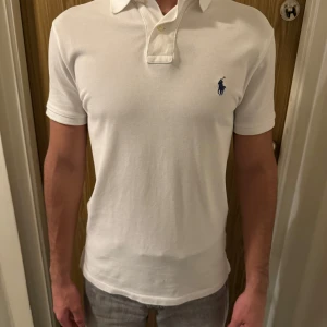 Vit kortärmad pikétröja från Ralph Lauren - Säljer en stilren vit pikétröja från Ralph Lauren i nyskick. Den har en klassisk krage och korta ärmar, perfekt för både vardag och fest. Tröjan är i bomull och har den ikoniska loggan broderad på bröstet. Passar perfekt för sommaren! Nypris 1400kr