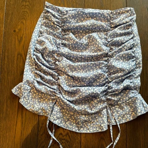 Blommig kjol från Shein - Säljer en superfin blommig kjol från Shein i storlek M. Kjolen är blå med små vita blommor och har en söt volangdetalj längst ner. Perfekt för vår och sommar! 🌸