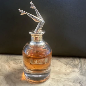 Scandal parfymflaska - Säljer en cool parfymflaska från Jean Paul Gaultier med namnet Scandal. Flaskan har en unik design med ett par silverfärgade ben som lock. Parfymen är i en varm, bärnstensfärgad nyans och flaskan är rund och elegant. Perfekt för den som vill ha något annorlunda på sminkbordet!